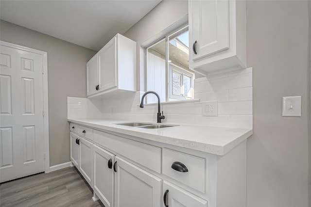 kitchen with a sink, light wood-style floors, tasteful backsplash, and white cabinets