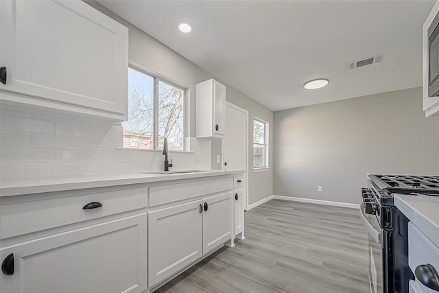 kitchen with black gas range oven, visible vents, backsplash, white cabinets, and a sink