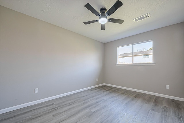 empty room featuring a textured ceiling, wood finished floors, visible vents, and baseboards