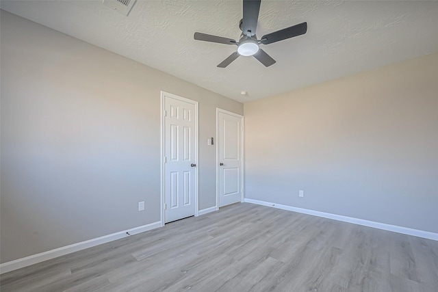 empty room featuring baseboards, visible vents, light wood finished floors, and a textured ceiling