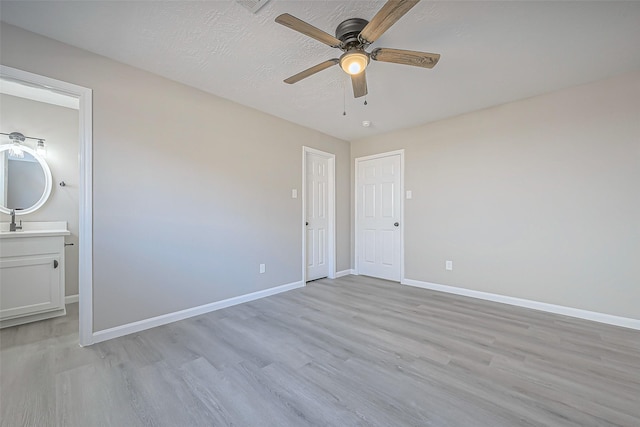 unfurnished bedroom featuring light wood-type flooring, ensuite bathroom, a textured ceiling, baseboards, and ceiling fan