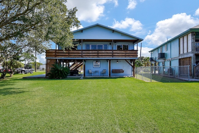 back of house with a wooden deck, a lawn, stairs, and fence