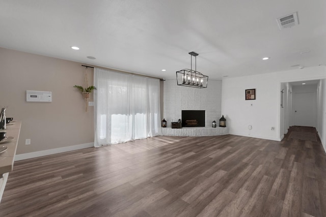 unfurnished living room with a brick fireplace, recessed lighting, visible vents, and dark wood-style flooring