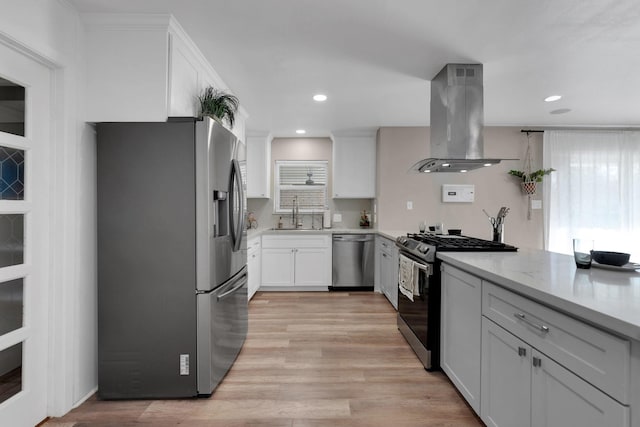 kitchen with light wood finished floors, island range hood, white cabinets, stainless steel appliances, and a sink