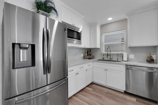 kitchen featuring recessed lighting, a sink, stainless steel appliances, white cabinets, and light wood-style floors