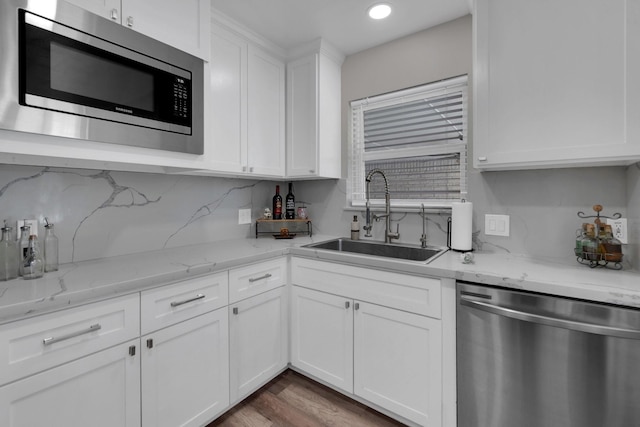 kitchen with decorative backsplash, appliances with stainless steel finishes, wood finished floors, white cabinets, and a sink