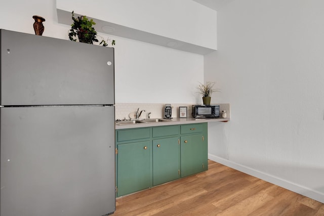 kitchen featuring light wood finished floors, freestanding refrigerator, a sink, black microwave, and green cabinets