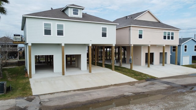 beach home with a carport, a garage, driveway, and roof with shingles