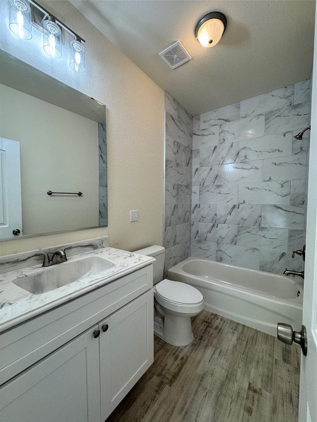 bathroom featuring visible vents, toilet, wood finished floors, a textured wall, and vanity