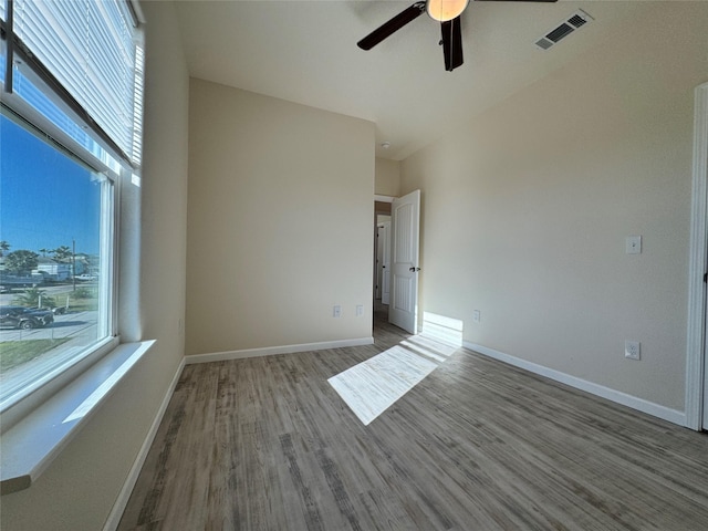 spare room with ceiling fan, visible vents, baseboards, and wood finished floors