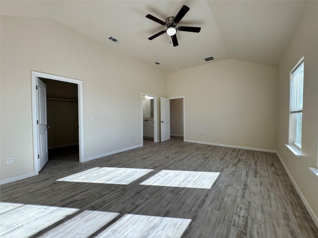 unfurnished bedroom with wood finished floors, visible vents, baseboards, lofted ceiling, and a walk in closet