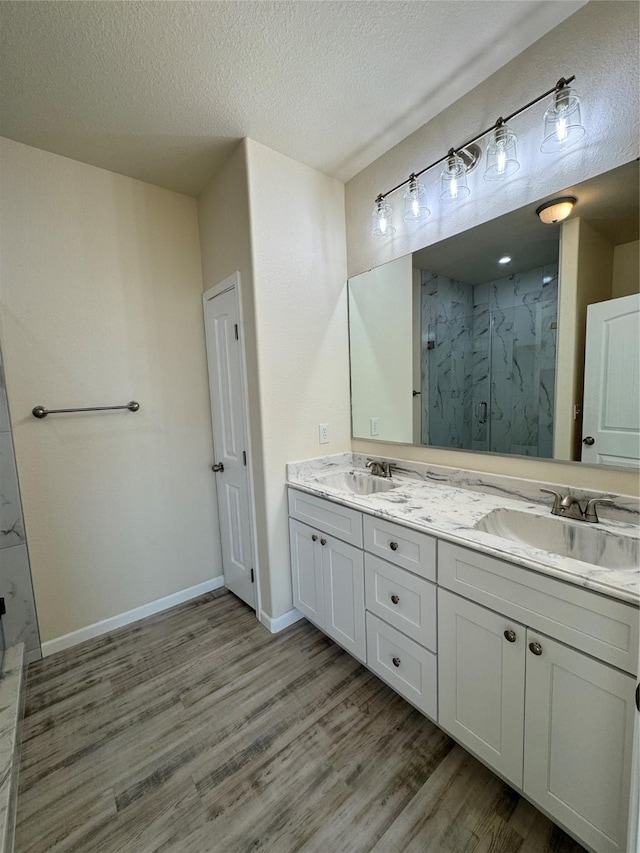 bathroom featuring a textured ceiling, wood finished floors, a marble finish shower, and a sink