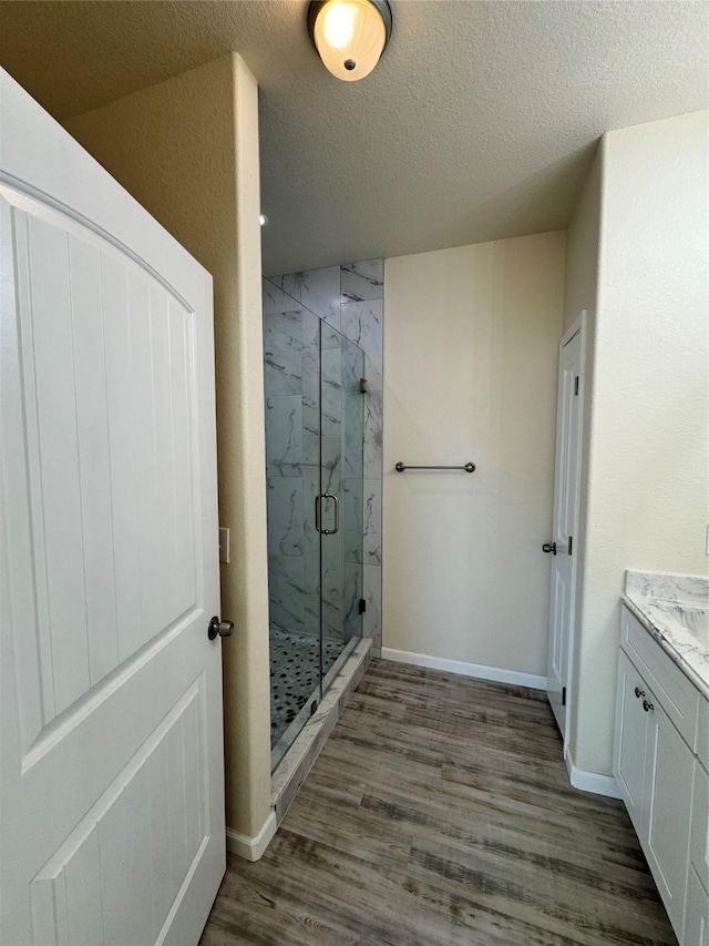 full bath featuring a marble finish shower, a textured ceiling, baseboards, and wood finished floors