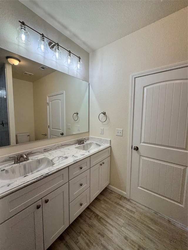 bathroom featuring a sink, a textured ceiling, wood finished floors, and double vanity