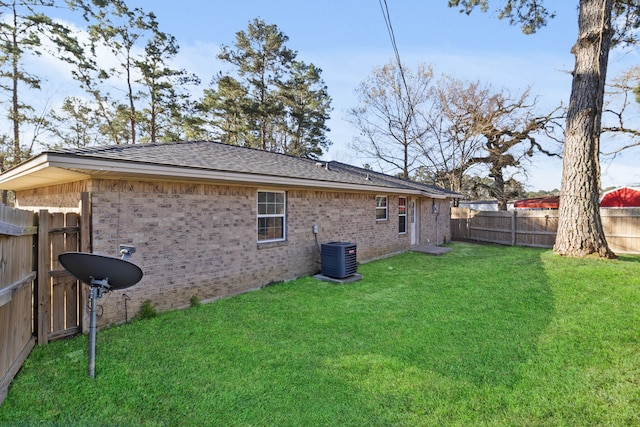 rear view of property featuring brick siding, a shingled roof, central AC, a lawn, and a fenced backyard