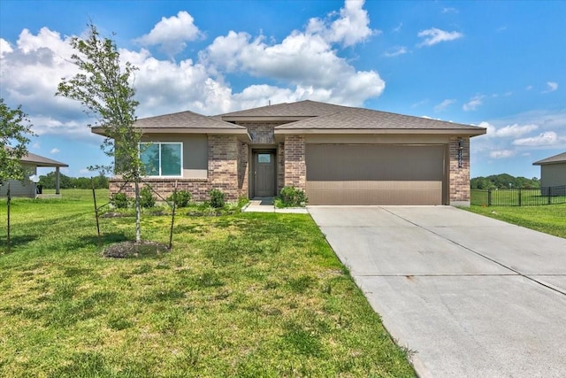 prairie-style house with fence, concrete driveway, a front yard, an attached garage, and brick siding