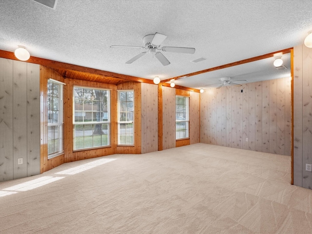 carpeted spare room with wooden walls, visible vents, a textured ceiling, and ceiling fan