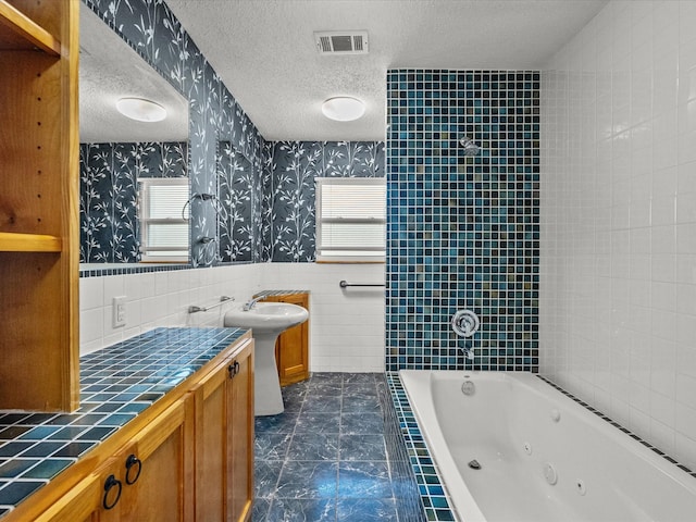 bathroom with visible vents, a textured ceiling, wainscoting, and wallpapered walls