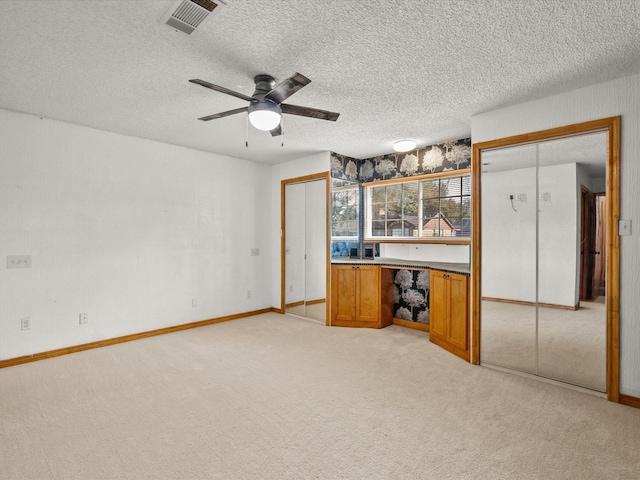 interior space featuring visible vents, light colored carpet, a ceiling fan, and a textured ceiling