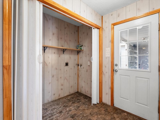 washroom featuring stone finish flooring, a textured ceiling, wooden walls, hookup for a washing machine, and laundry area