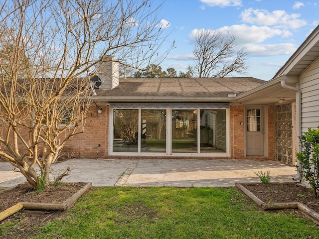 rear view of property with a patio, a lawn, brick siding, and a chimney