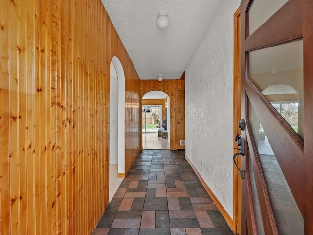 hall with arched walkways, wood walls, and a textured ceiling