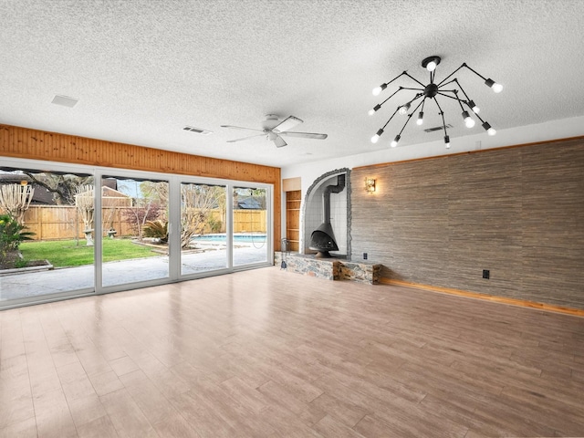 unfurnished living room with wooden walls, wood finished floors, visible vents, a wood stove, and a textured ceiling