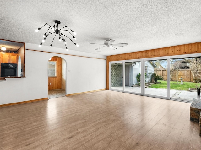 unfurnished living room with light wood-type flooring, arched walkways, a textured ceiling, and a ceiling fan