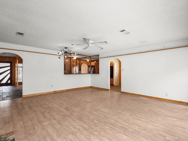 unfurnished living room with visible vents, a ceiling fan, a textured ceiling, arched walkways, and light wood finished floors