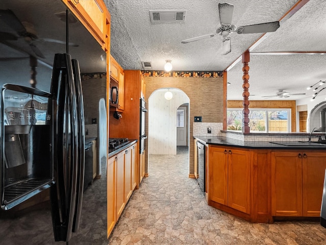 kitchen with dark countertops, visible vents, brown cabinets, arched walkways, and black appliances