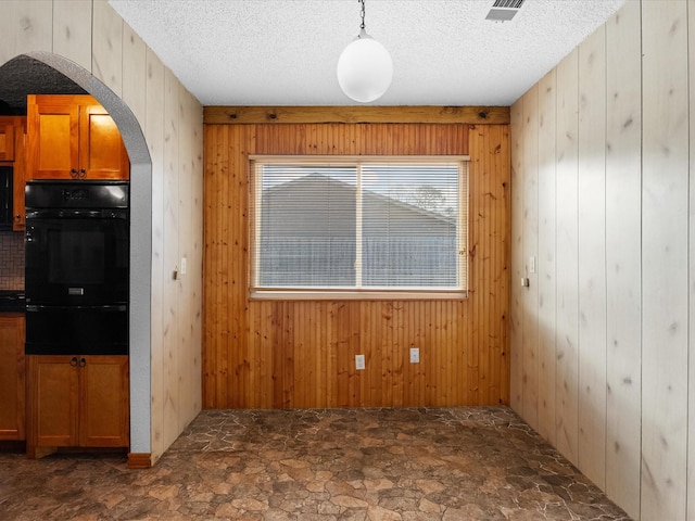 unfurnished dining area featuring a textured ceiling, wooden walls, arched walkways, and stone finish flooring