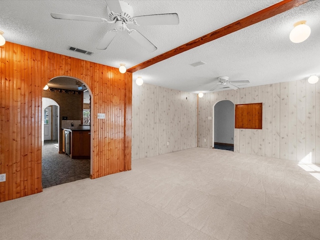 spare room featuring carpet, visible vents, beam ceiling, arched walkways, and ceiling fan