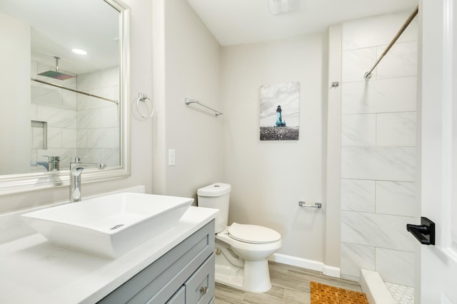 bathroom featuring toilet, wood finished floors, tiled shower, baseboards, and vanity