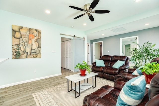 living room featuring visible vents, ceiling fan, baseboards, a barn door, and wood finished floors