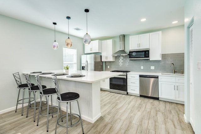 kitchen with visible vents, a sink, white cabinetry, stainless steel appliances, and wall chimney exhaust hood