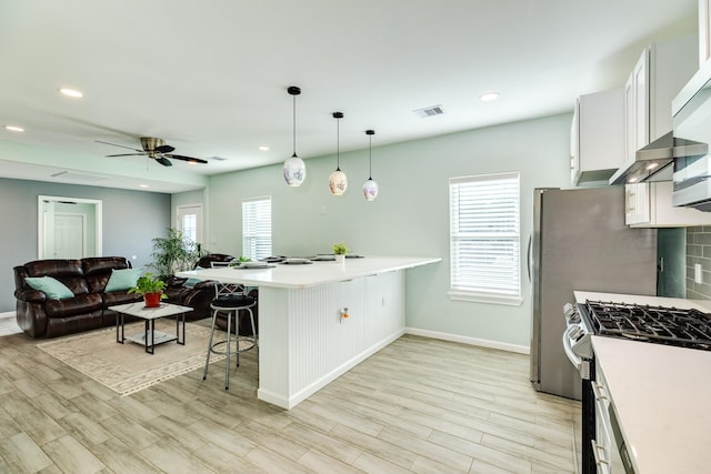 kitchen featuring stainless steel gas range oven, a peninsula, a breakfast bar area, and a wealth of natural light