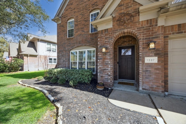 view of exterior entry with a garage and brick siding