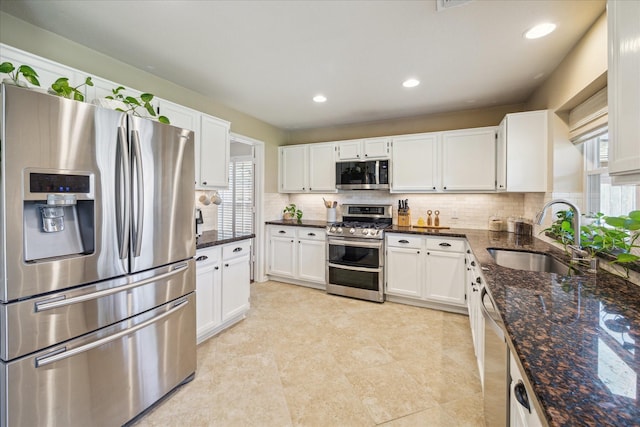 kitchen featuring dark stone counters, backsplash, appliances with stainless steel finishes, and a sink