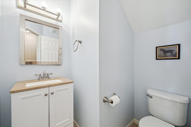 half bathroom featuring toilet, vanity, baseboards, and vaulted ceiling