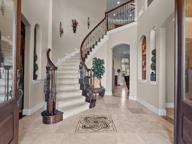 foyer featuring stairs, a high ceiling, arched walkways, and baseboards