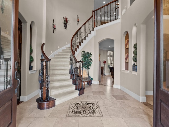 foyer entrance featuring arched walkways, stairs, baseboards, and a high ceiling