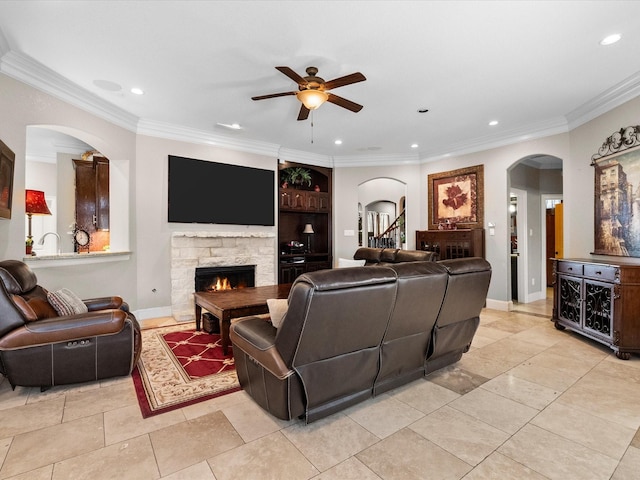 living room featuring ceiling fan, arched walkways, crown molding, and a stone fireplace