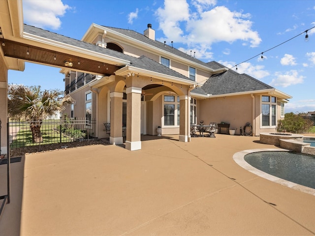 rear view of house with a chimney, fence, a shingled roof, a patio, and stucco siding