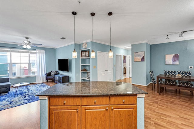 kitchen with brown cabinetry, visible vents, light wood-style flooring, and hanging light fixtures