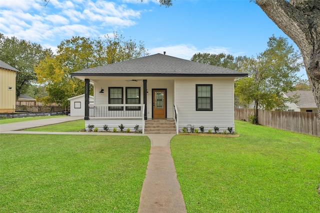 bungalow with fence, covered porch, ceiling fan, a shingled roof, and a front lawn