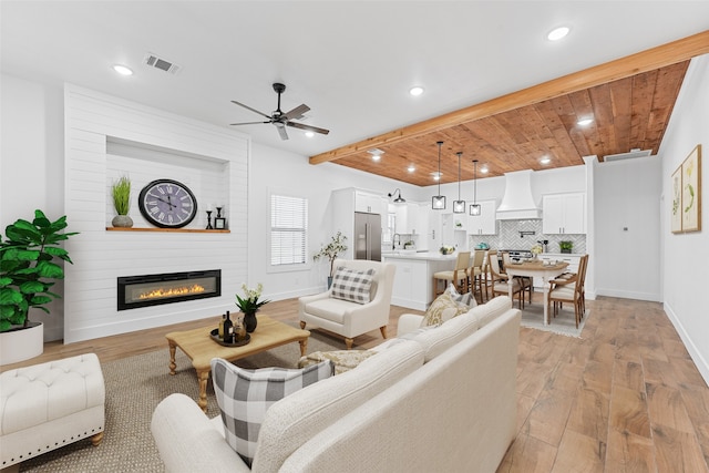 living area featuring baseboards, visible vents, beamed ceiling, light wood-type flooring, and a large fireplace