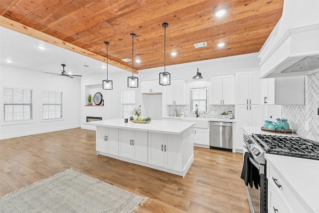 kitchen with a ceiling fan, stainless steel appliances, wooden ceiling, a fireplace, and custom exhaust hood