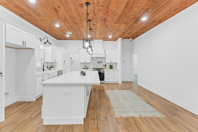 kitchen with stainless steel gas range oven, custom range hood, backsplash, light countertops, and wood ceiling