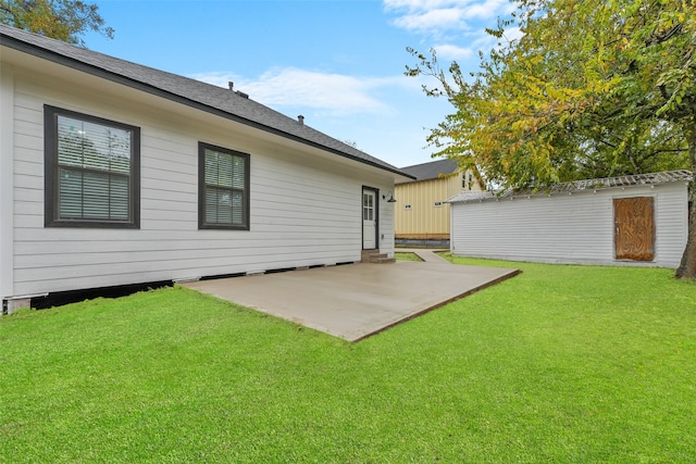 rear view of property featuring a patio, roof with shingles, a yard, an outdoor structure, and a storage unit