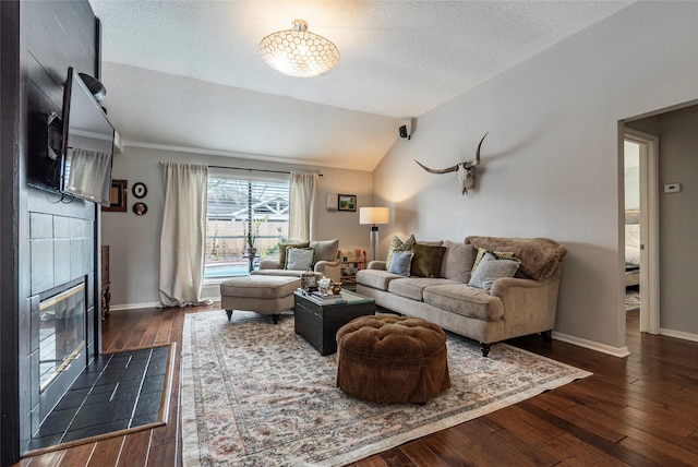 living room featuring baseboards, lofted ceiling, wood-type flooring, and a tiled fireplace